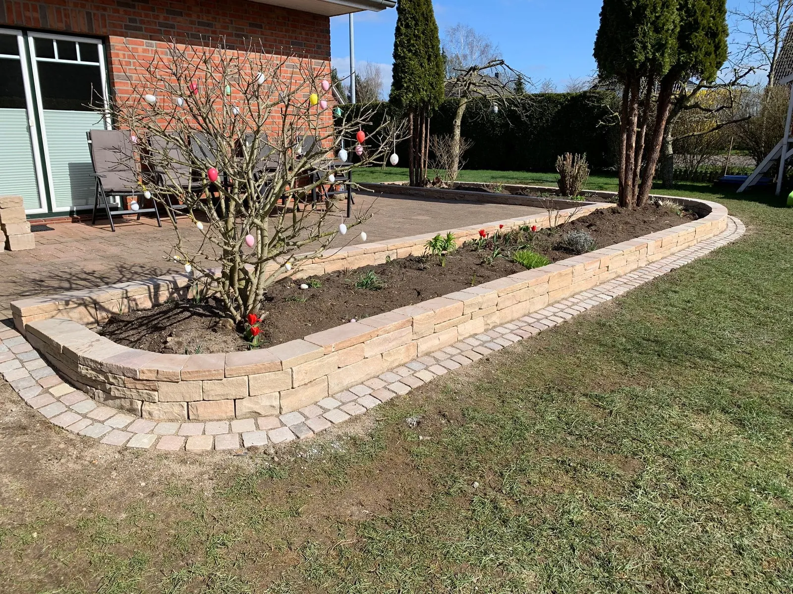 Geschwungenes Beet mit Natursteinmauer und Pflastereinfassung am Rasen