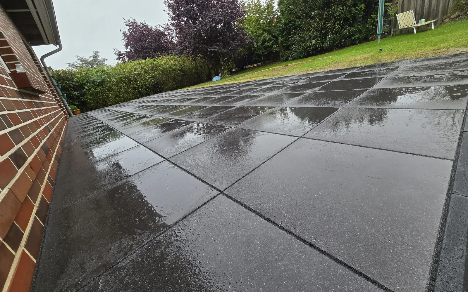 Dunkle Terrassenplatten entlang eines Klinkerhauses